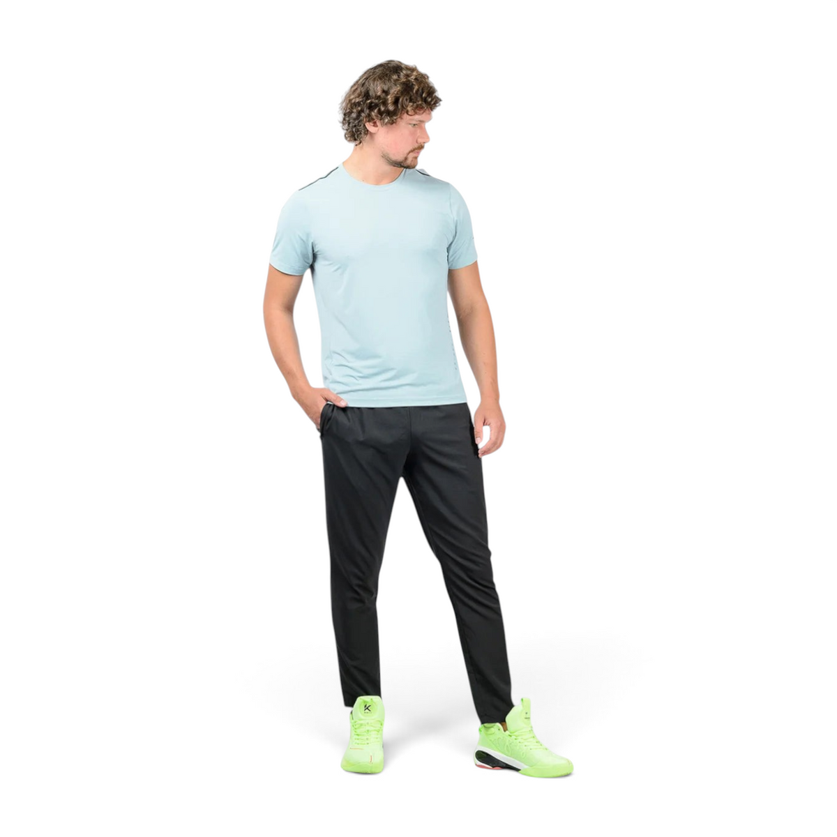 A man wearing FRG black ankle pants and a light blue t-shirt with bright neon green athletic sneakers