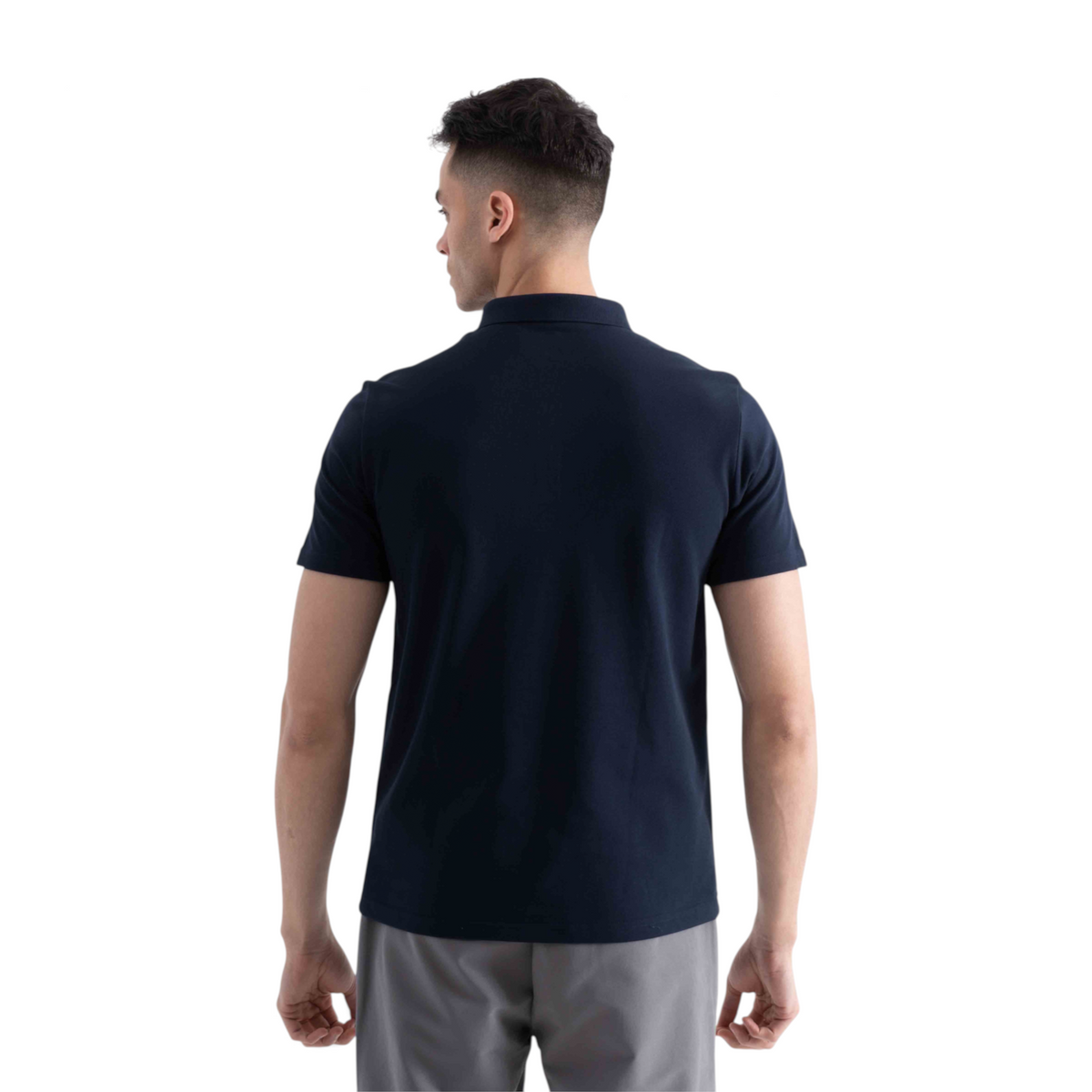 Back view of a man wearing a navy blue FRG short sleeve polo shirt with grey trousers against a white background
