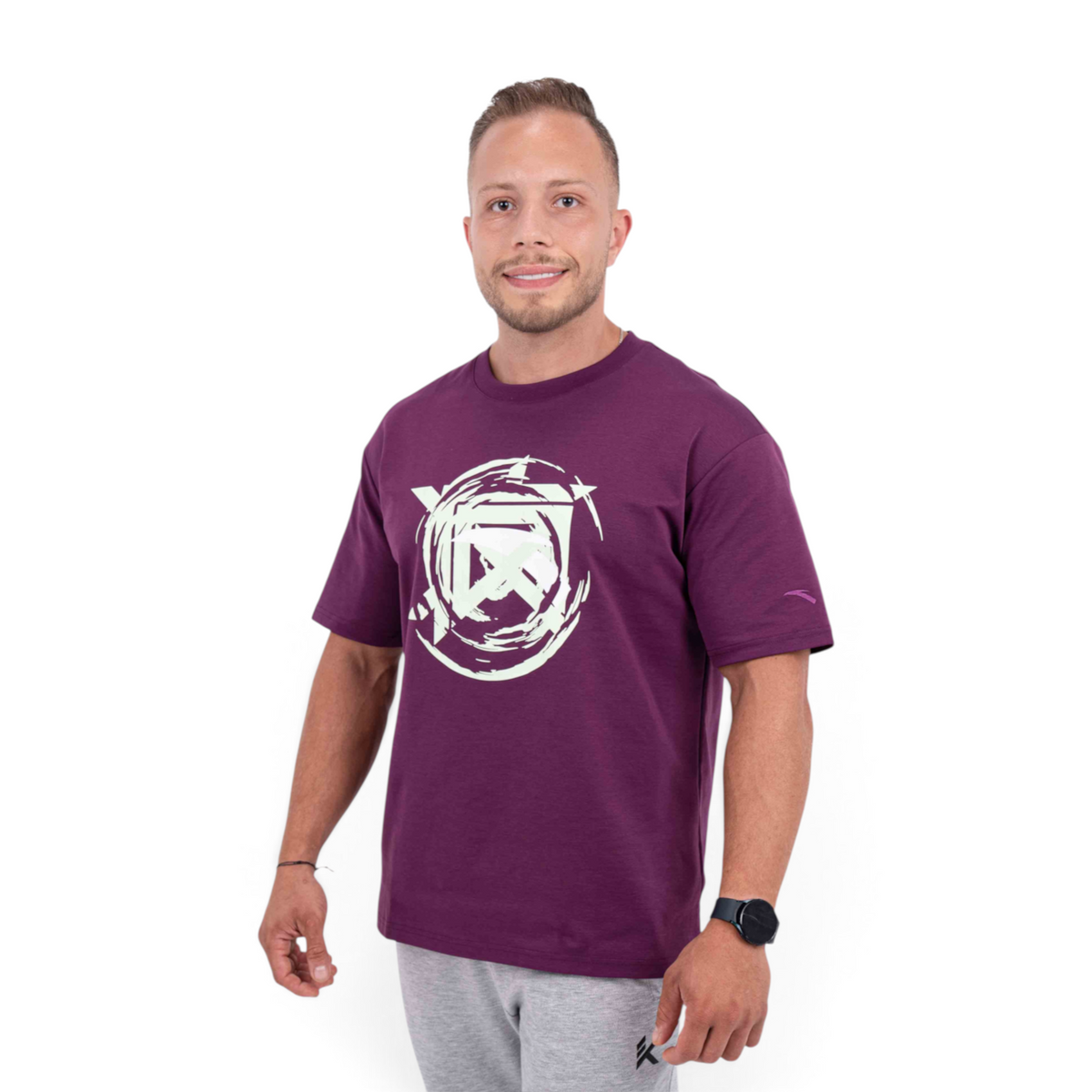 A man wearing a purple FRG T-shirt with a white abstract circular graphic print on the chest, studio shot.