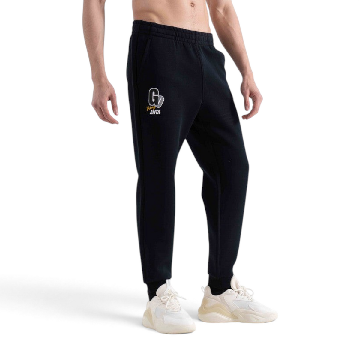 FRG black knit track pants featuring a white and yellow graphic logo on the thigh, worn by a man with white sneakers