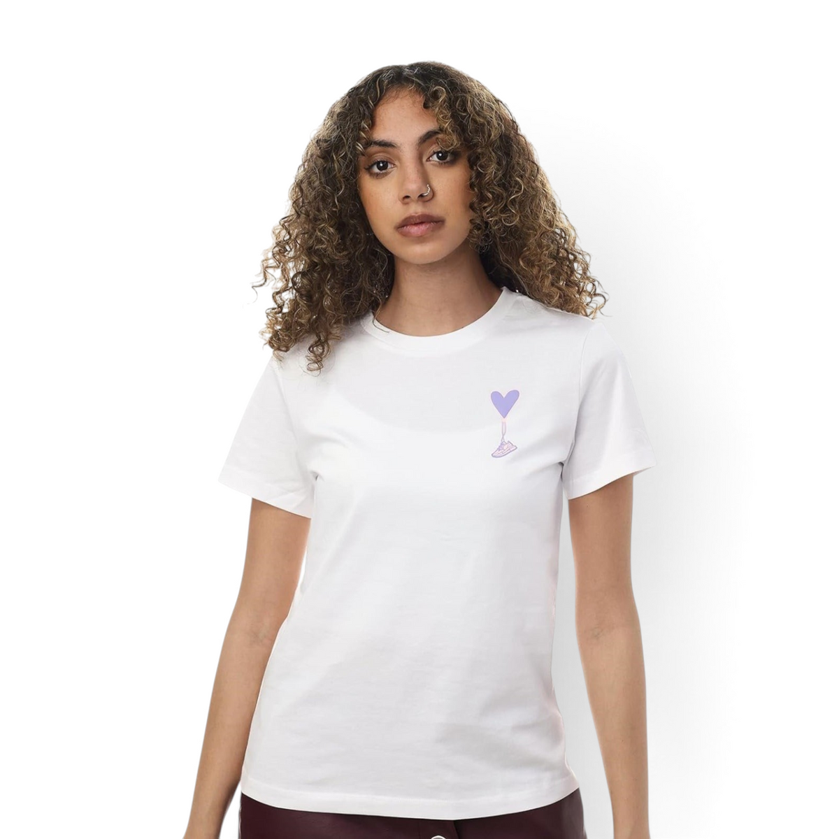 A woman wearing a white FRG T-shirt featuring a small purple heart balloon graphic on the chest.