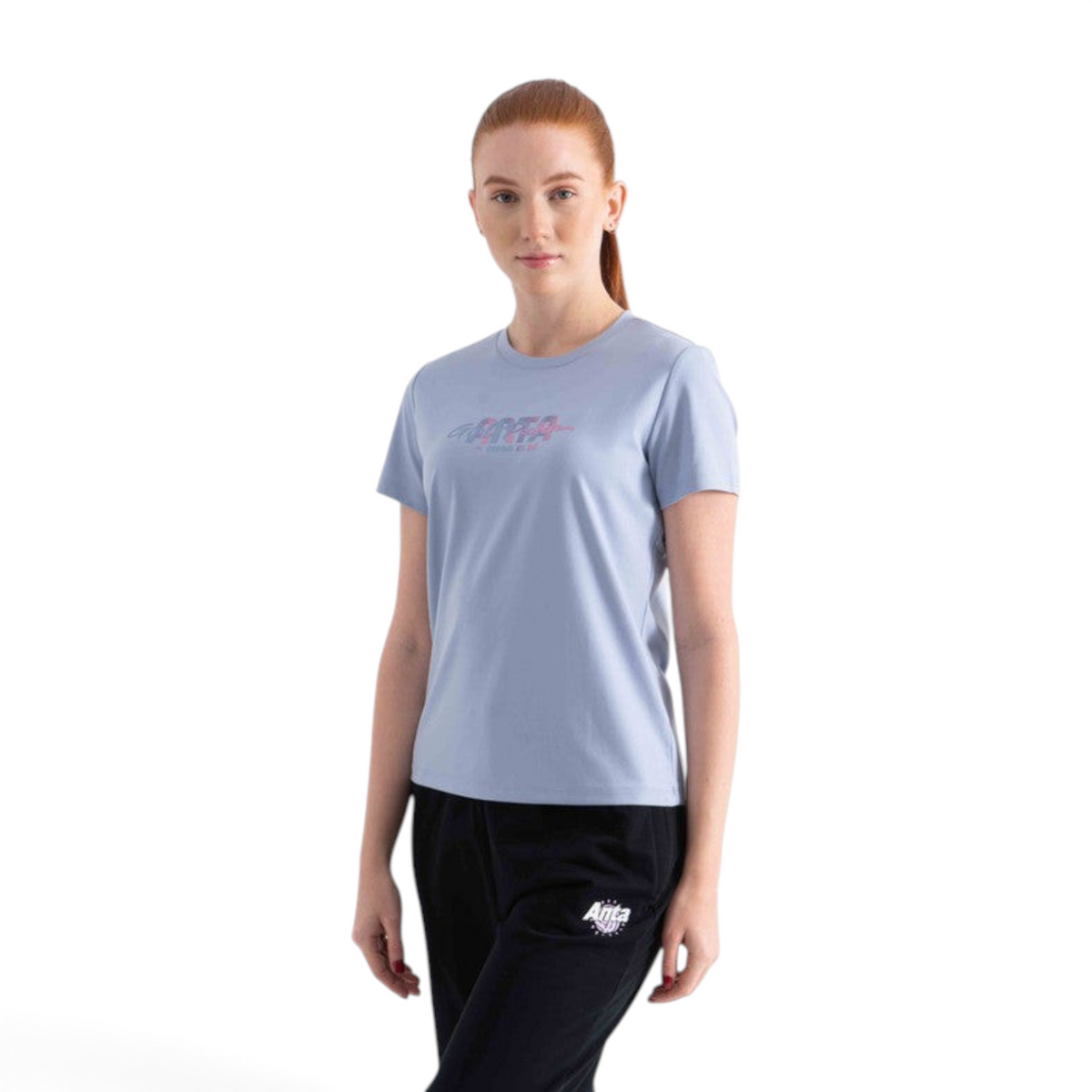 A woman wearing a light blue FRG SS TEE with a graphic logo print on the chest, paired with black athletic pants.