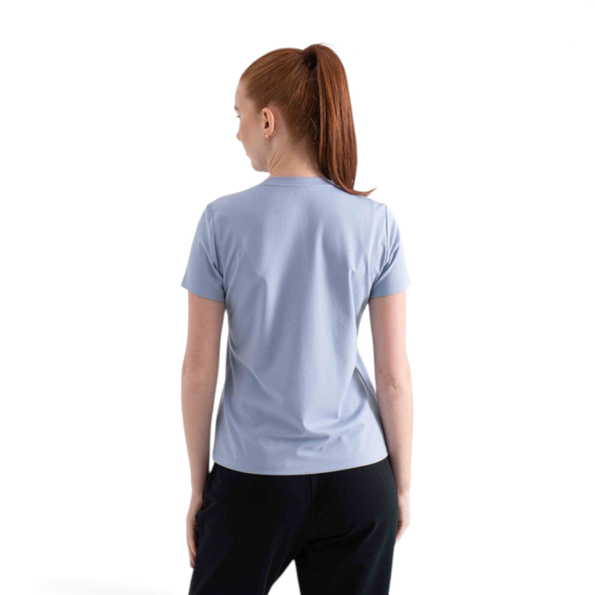 Back view of a woman wearing a light blue FRG short sleeve t-shirt with black pants against a white background