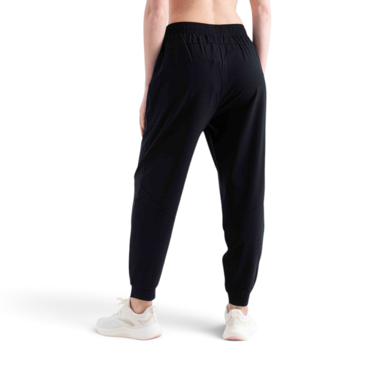 Back view of a woman wearing FRG black knit ankle pants with an elastic waistband and cuffs, paired with sneakers.