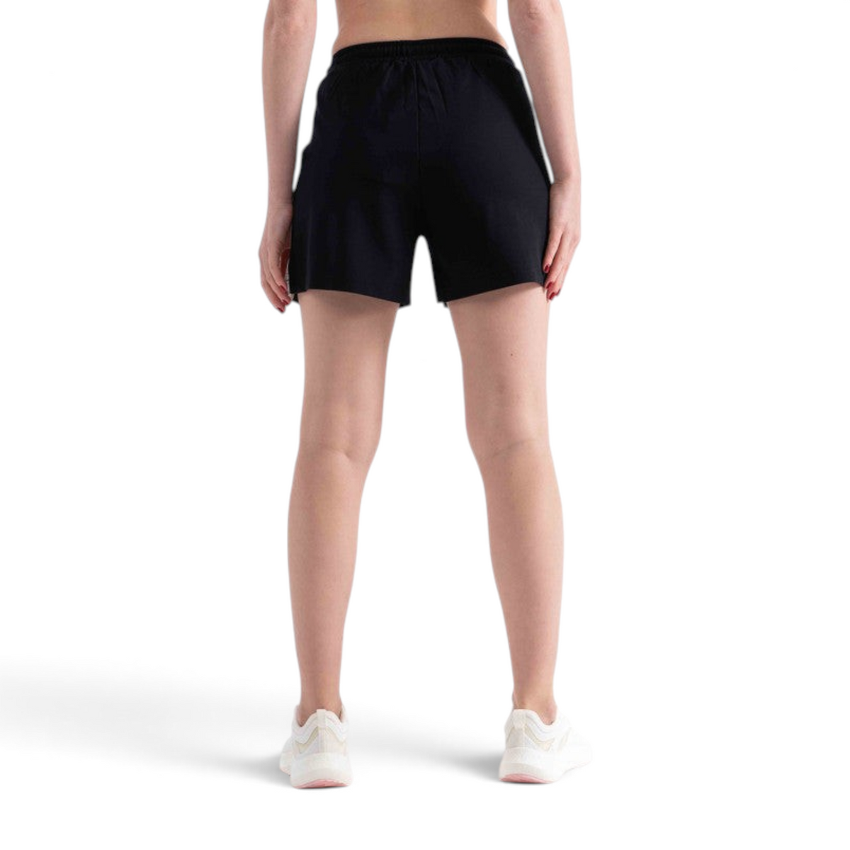 Back view of a woman wearing black FRG knit shorts with an elastic waistband, paired with white athletic sneakers.