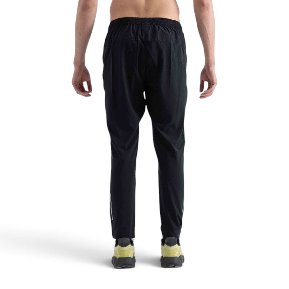 Back view of a man wearing black FRG WOVEN TRACK PANTS with an elastic waistband and reflective detailing.