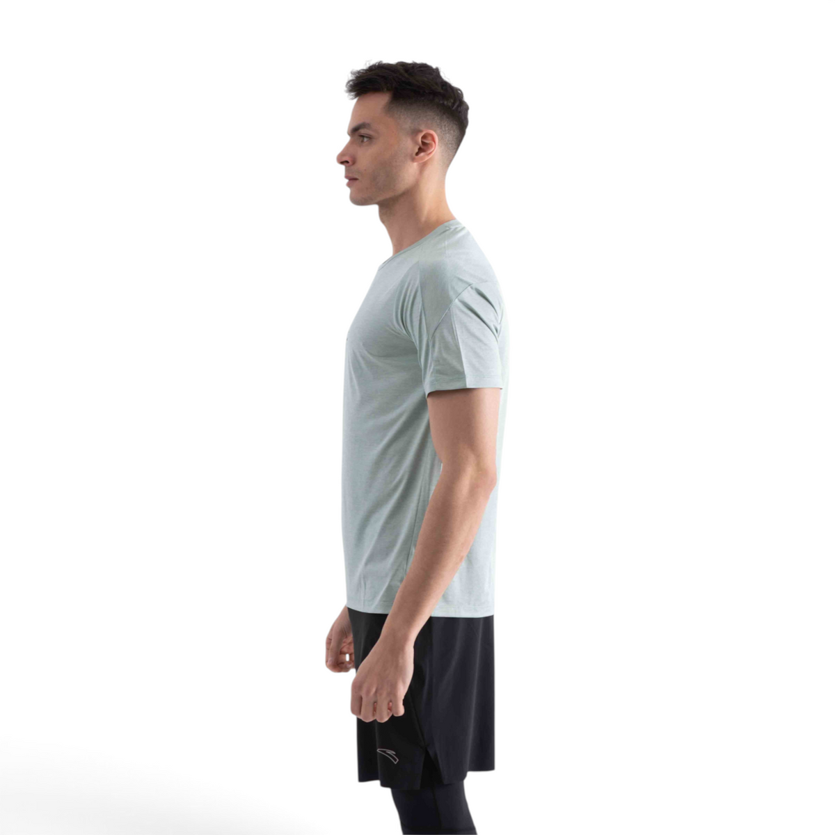 A man wearing a light sage green FRG short sleeve t-shirt and black athletic shorts in a side profile view.
