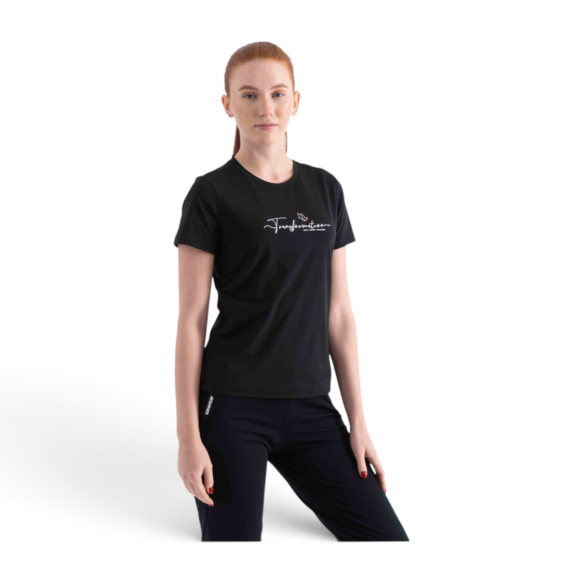 A woman wearing a black FRG regular fit polyester t-shirt with white Transformation script text on the chest.
