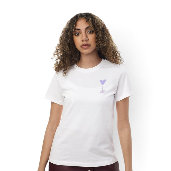 A woman wearing a white FRG T-shirt featuring a small purple heart balloon graphic on the chest.