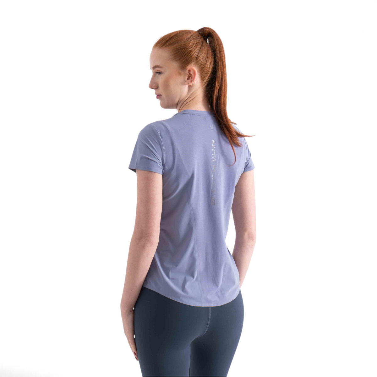 FRG SS TEE in light purple worn by a woman, showing the back view with a vertical reflective logo detail.