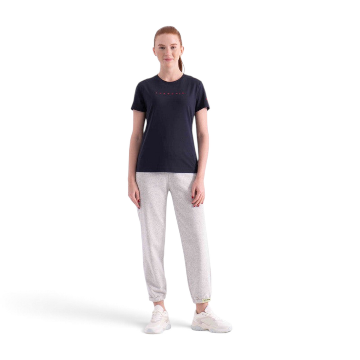 A woman wearing a black FRG short-sleeve t-shirt with red lettering paired with grey sweatpants and white sneakers.